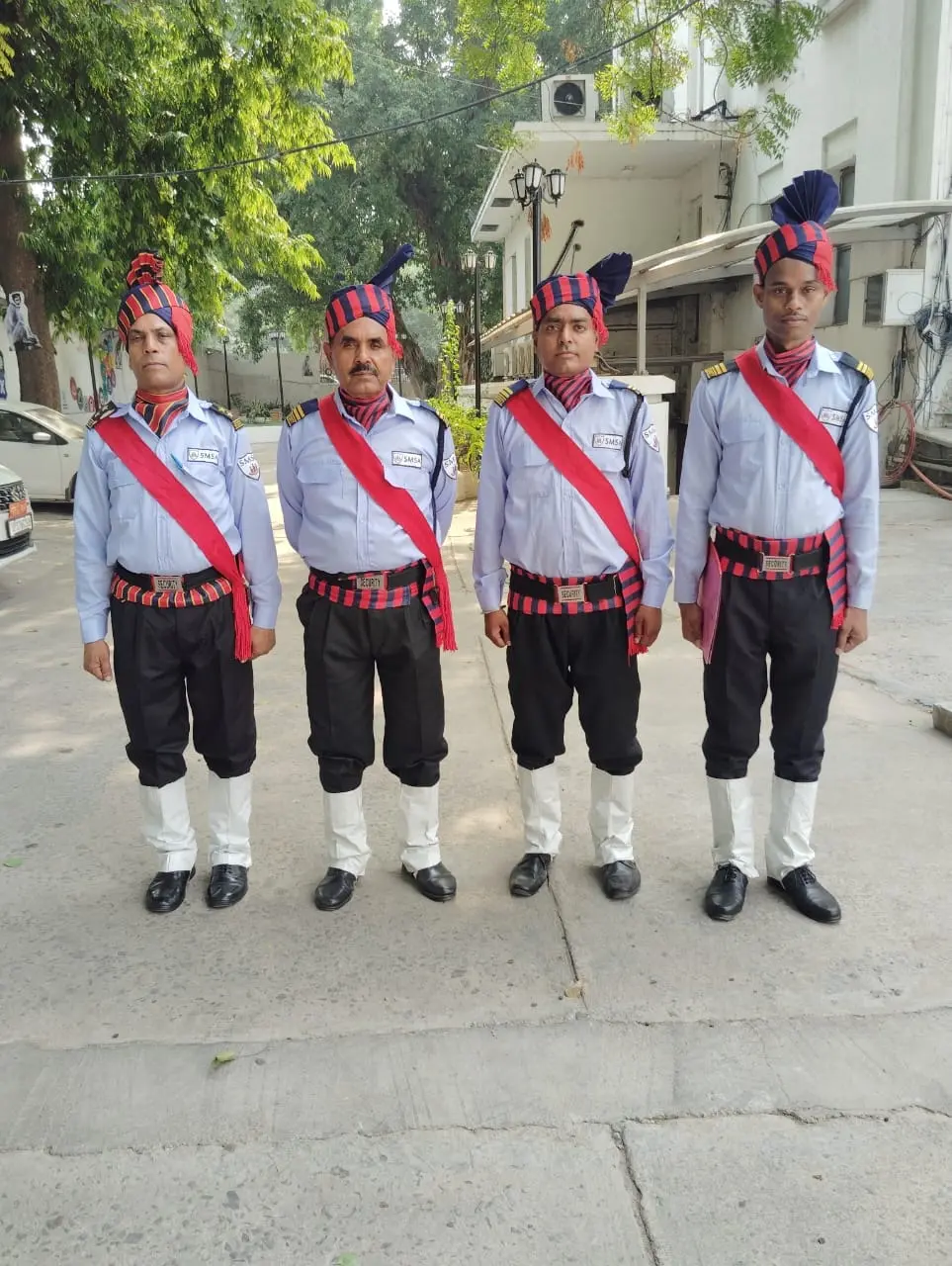 Four SMSA security guards in ceremonial uniform with red sashes at a client gate