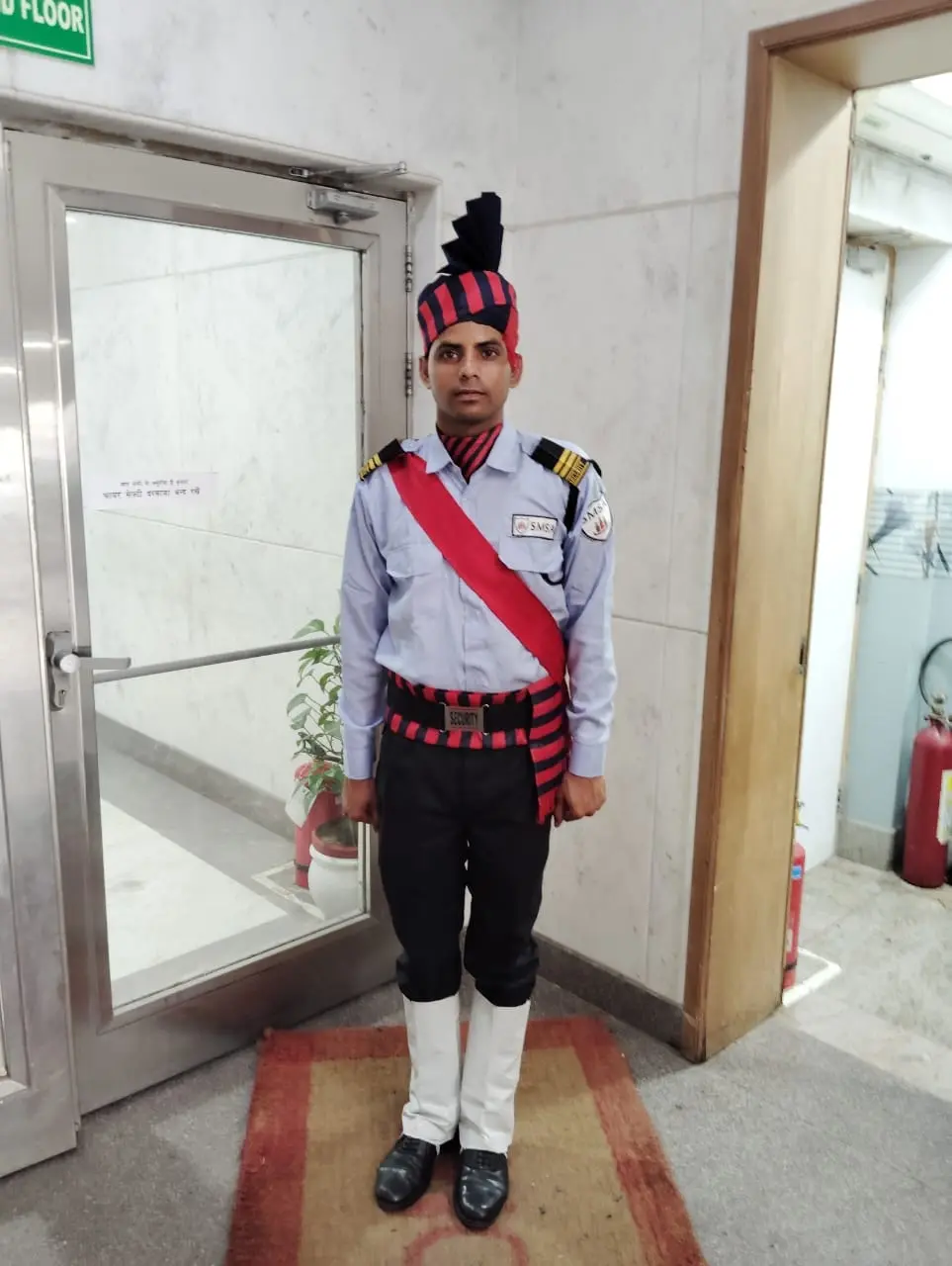 An SMSA guard in ceremonial uniform standing at attention beside a glass entrance door