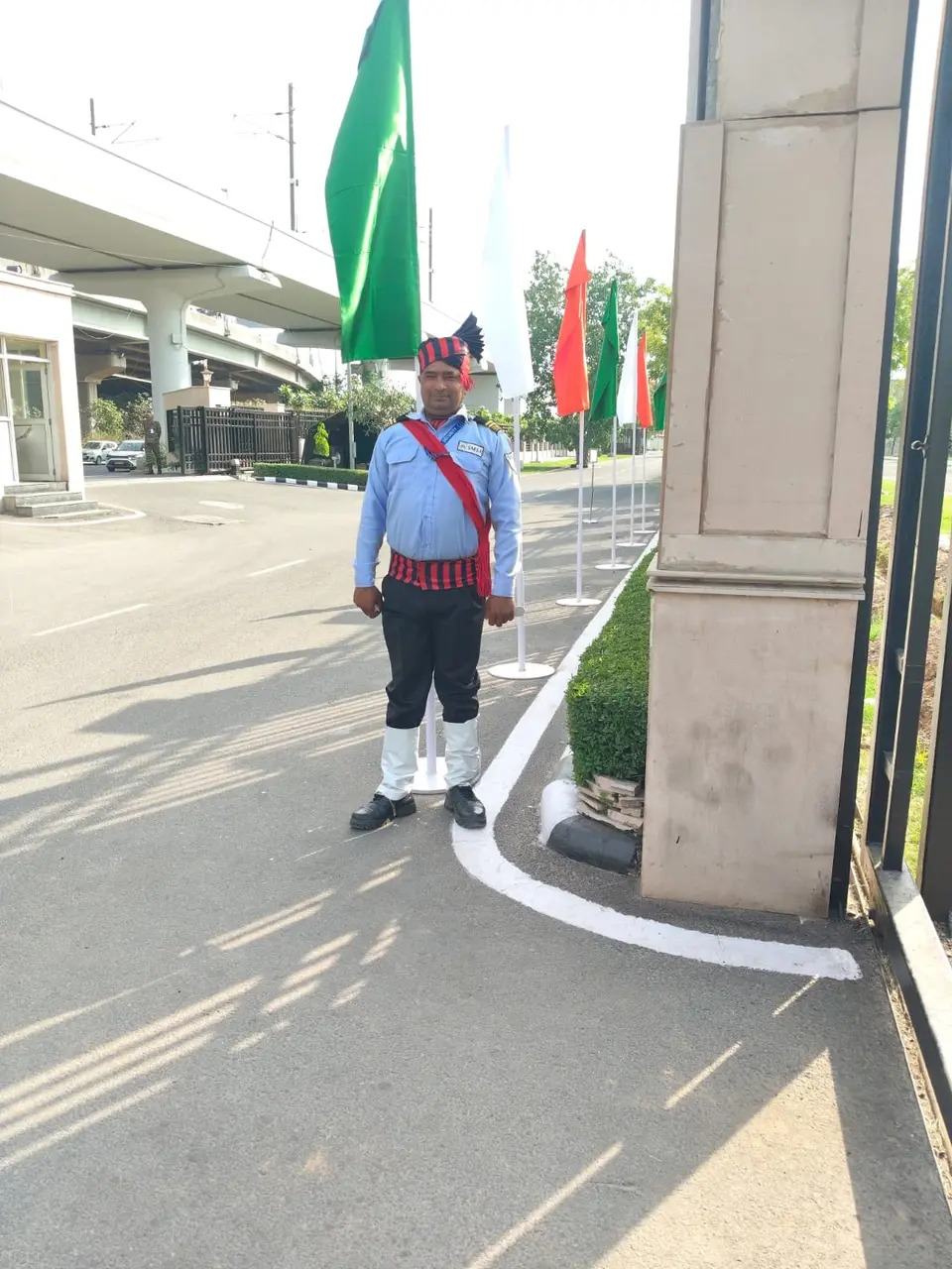 An SMSA guard in ceremonial uniform on post by a gate with flags in the background