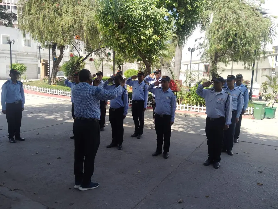 Security guards in light blue uniforms practicing a synchronized salute in front of their instructor