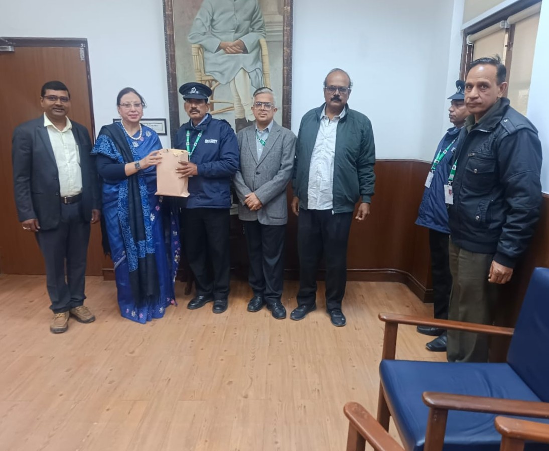 Principal handing a gift bag to a security guard during a felicitation ceremony